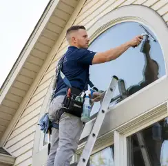 Professional window cleaner on a ladder using a squeegee to clean an exterior arched window, Reno, NV.